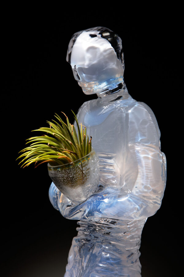 A sculpture celebrates the studios achievements in running off renewable energy, created by Allister Malcolm in opalescent glass a figure holding a glass vessel contains a tillandsia plant