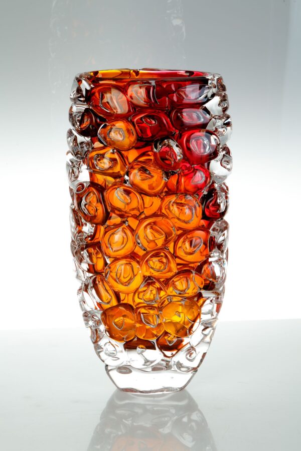 a glass vase covered in glass bubbles in orange and red tones looks like glass bubblewrap.